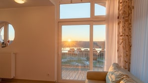 Ein Zimmer mit einer großen Schiebeglastür, die auf eine Terrasse führt, einem runden Spiegel an der Wand und einem beigefarbenen Sofa.