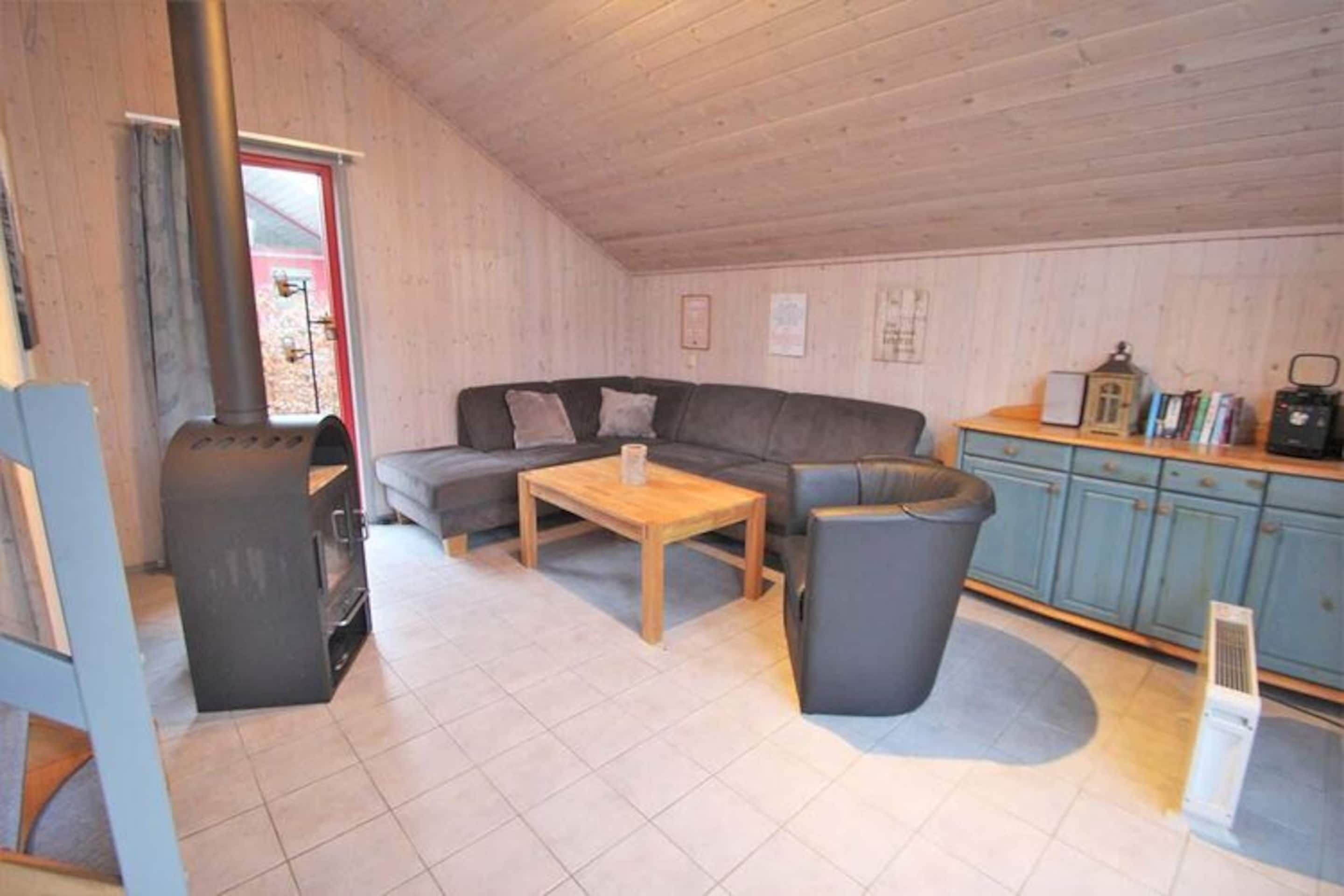 Ett mysigt rum med en soffa, ett litet bord, en papperskorg och en liten köksdel med skåp och en spis.