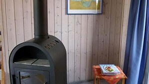 Un poêle à bois se trouve dans une pièce aux murs en bois, avec une petite table sur laquelle est posé un livre.