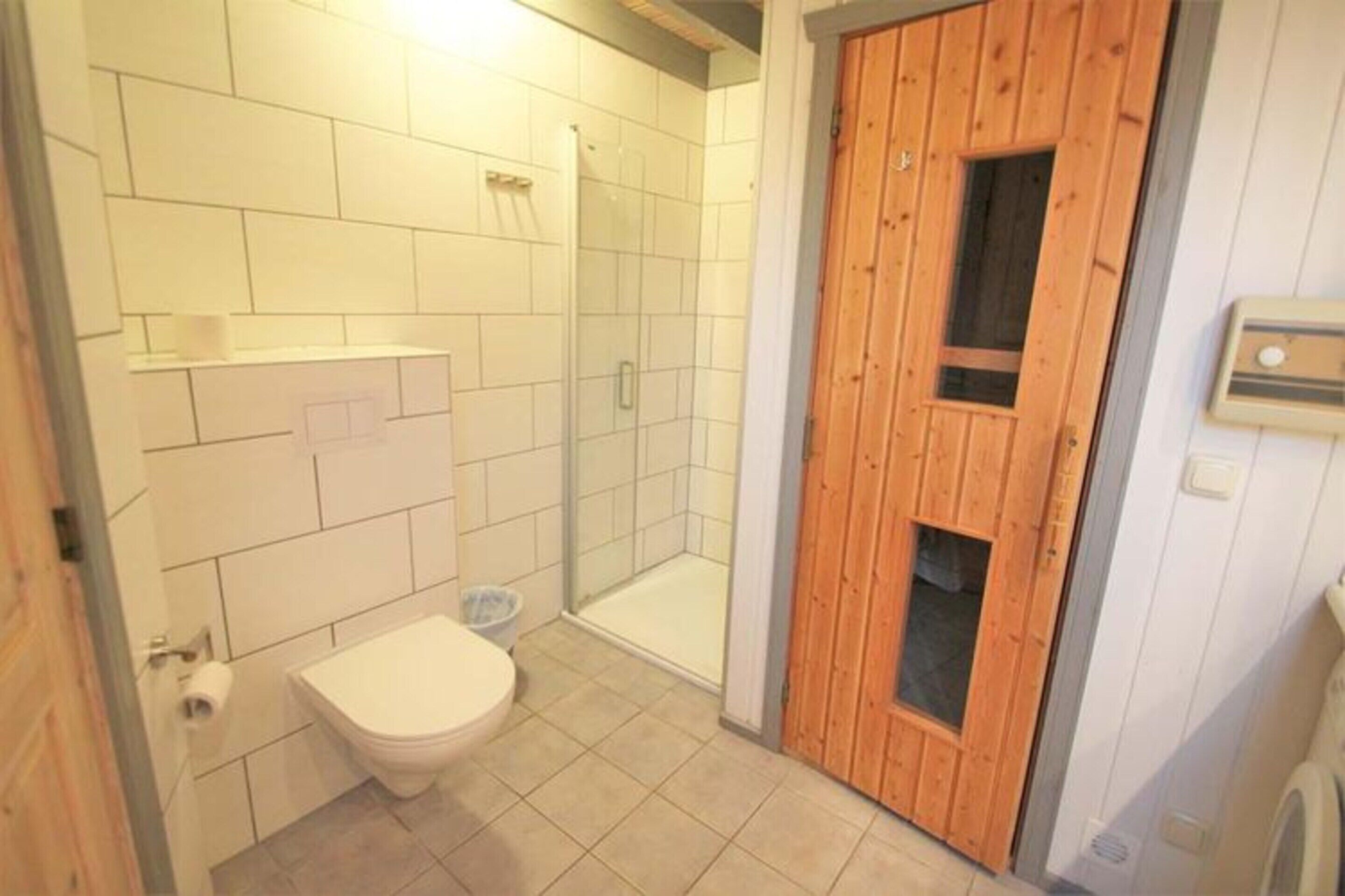 Une salle de bain avec des carreaux blancs, des toilettes, une douche en verre et une porte en bois.