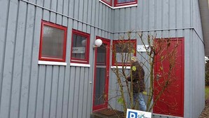 Un bâtiment gris avec des fenêtres à cadre rouge et une petite entrée.