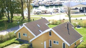 Ein gelbes, zweistöckiges Haus mit Schrägdach, umgeben von viel Grün und einer Marina mit Booten im Hintergrund.