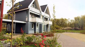 A two-story house with a balcony, surrounded by a garden with flowering plants. - Liebevoll Eingerichtetes Appartement (Rechlin)