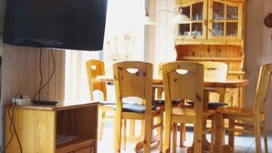 Ein Essbereich mit Holztisch und -stühlen, ein Fernseher an der Wand und eine Holzvitrine mit Glastüren.