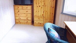 Ein Zimmer mit einem Holzschrank, einem Korbstuhl und einem Fenster.