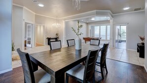 Un comedor amplio con una gran mesa de madera, varias sillas, una araña y vistas a otra habitación con mesa de billar.