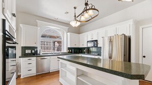 Una cocina con muebles blancos, encimera de granito, electrodomésticos de acero inoxidable y una araña.