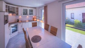 Une cuisine moderne avec des meubles blancs, une table à manger avec des chaises et une vue sur l’extérieur.
