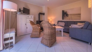 Un salon comprenant un canapé, deux fauteuils en osier, une table basse, un meuble et un téléviseur.