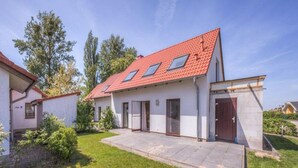 Une maison à deux étages, avec un toit recouvert de tuiles rouges, une terrasse couverte et un petit jardin.