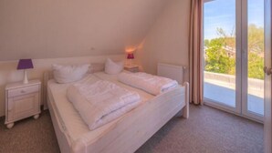 Une chambre avec un grand lit, une table de chevet, une lampe et une vue sur la verdure.