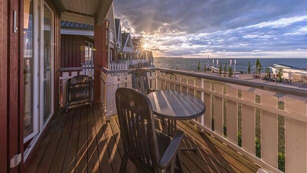 A wooden deck with a table and chairs, overlooking a coastal area with a sunset view. - Appartement im Ferienpark in Rechlin (Rechlin)