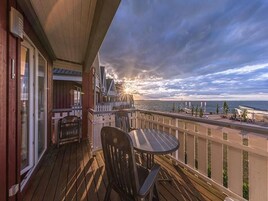 Una terraza de madera con una mesa y sillas, con vista a la costa y un atardecer.