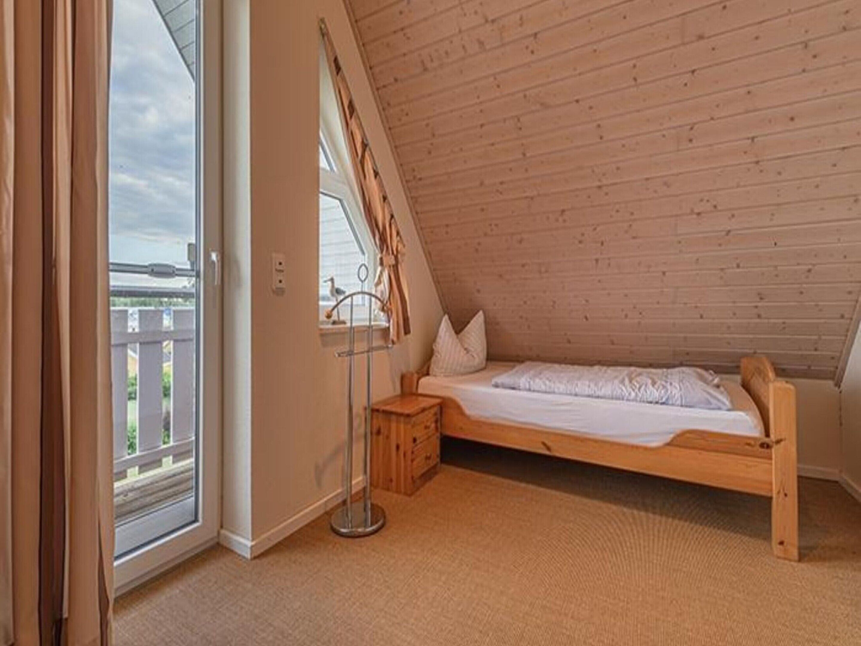 Un dormitorio con techo inclinado, una cama, un ventanal y vista a una terraza de madera.