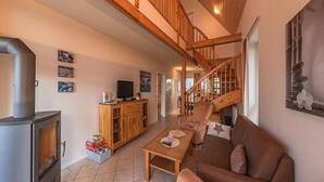 A spacious living area with a fireplace, wooden staircase, and a cozy sofa. - Appartement im Ferienpark in Rechlin (Rechlin)