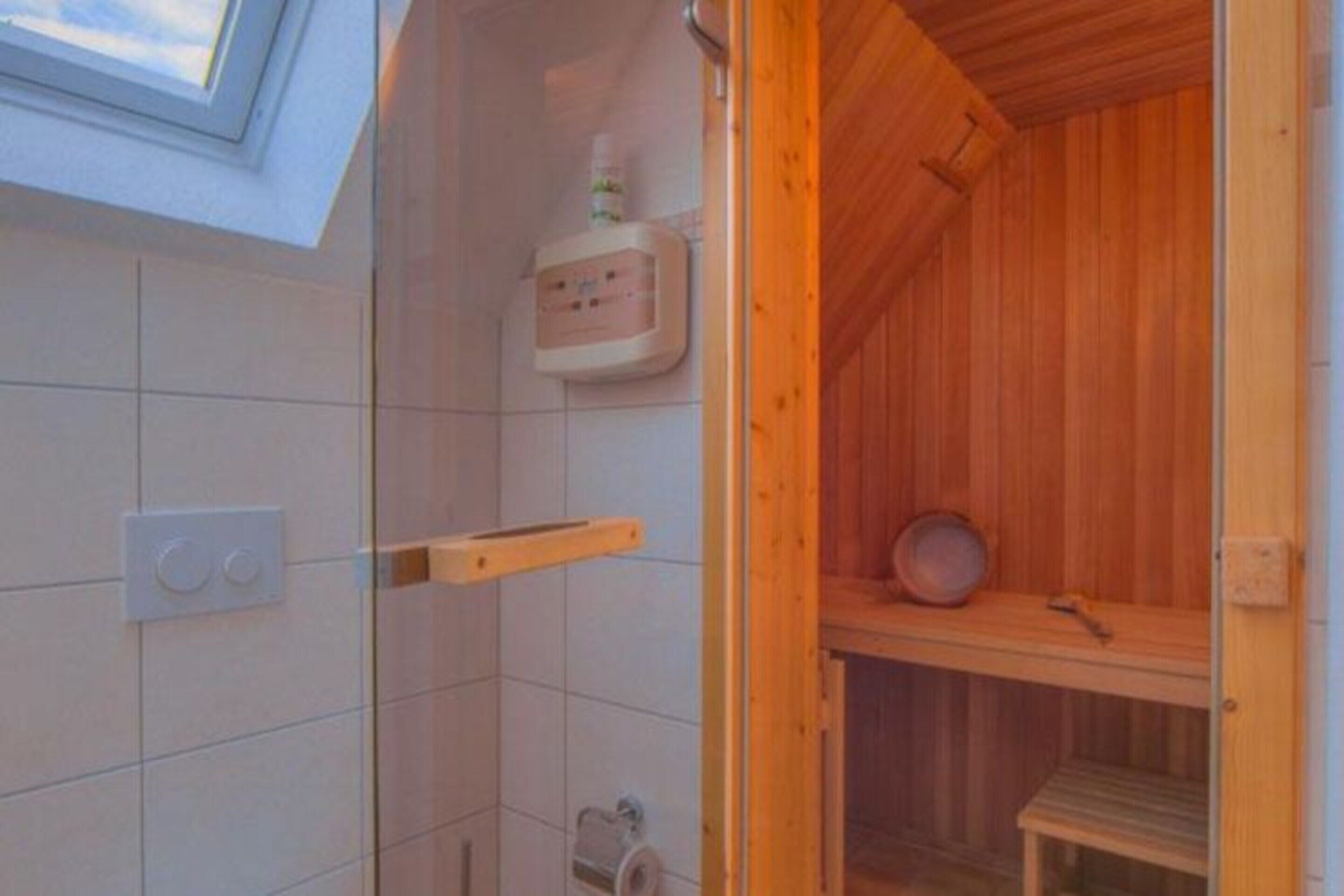 Un sauna en bois avec un espace de douche carrelé, une étagère avec un récipient et un panneau de commande.