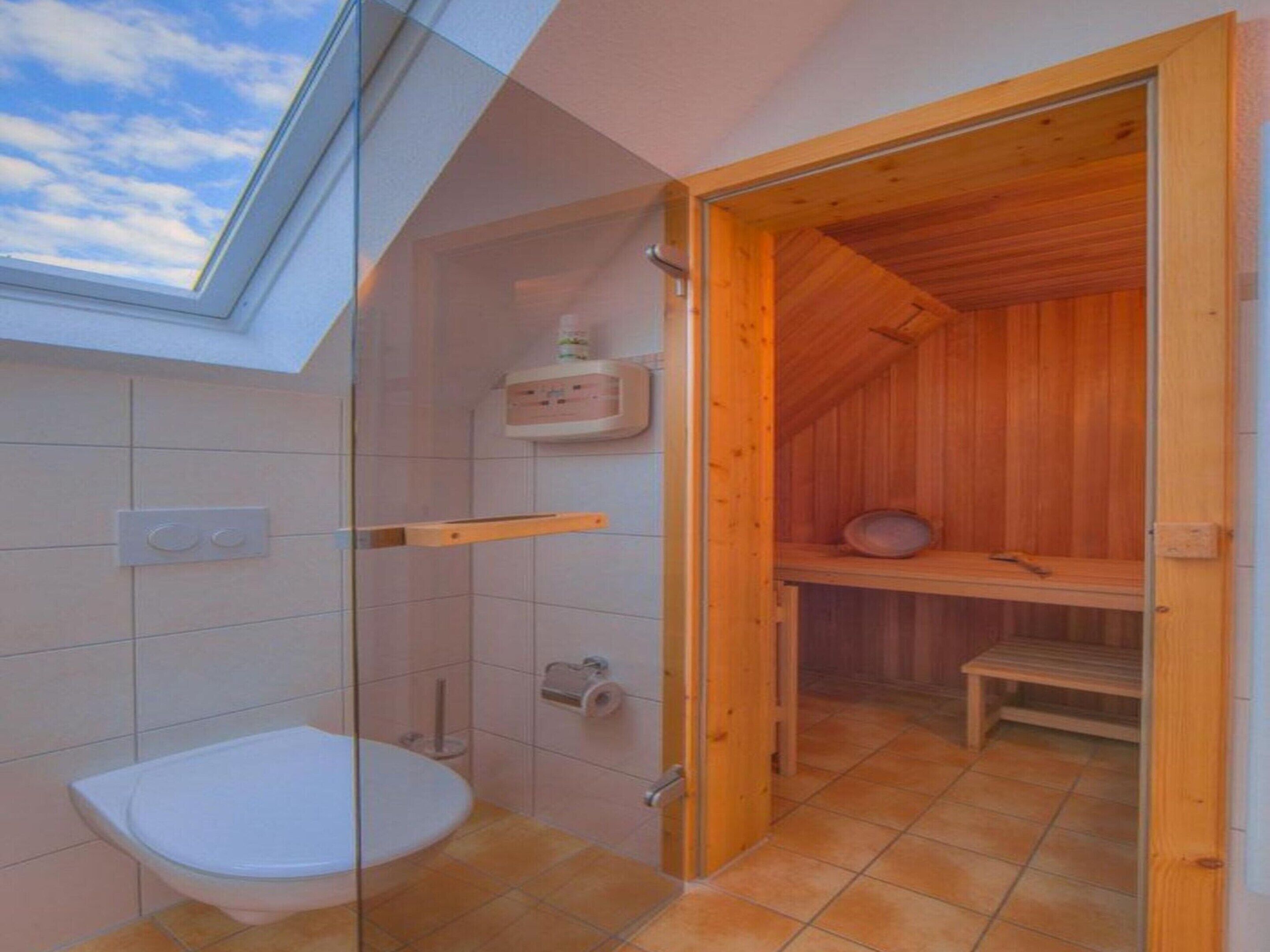Ein Badezimmer mit Duschkabine aus Glas, Toilette und einer Holzsauna.