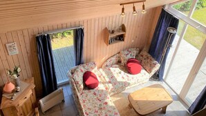 A cozy room with wooden walls, a bed with floral bedding and red pillows, a small wooden table, and a window with curtains. - Exklusives Skandinavisches Ferienhaus (Rechlin)