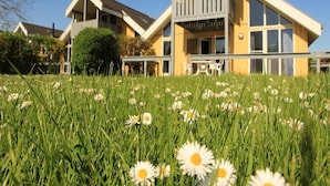 A two-story house with a balcony and a grassy lawn with daisies. - Exklusives Skandinavisches Ferienhaus (Rechlin)