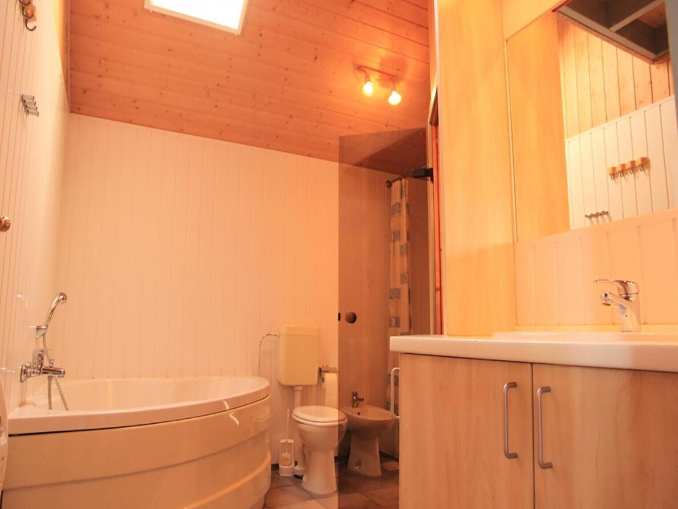 A bathroom with a wooden ceiling, a bathtub, a toilet, and a sink with a mirror.