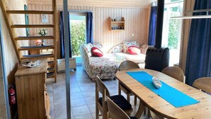 A cozy room with a wooden floor, a sofa with floral upholstery, a dining table with chairs, and a large window with curtains. - Exklusives Skandinavisches Ferienhaus (Rechlin)