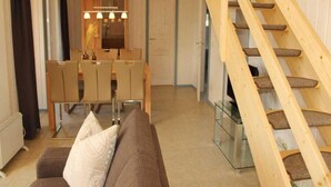 Ein Wohnzimmer mit braunem Sofa, einem Essbereich mit Tisch und Stühlen sowie einer Holztreppe.