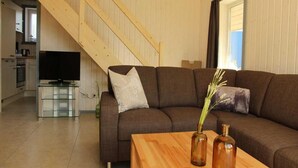 Ein Wohnzimmer mit einer braunen Couch, einem Holztisch und zwei Vasen. Im Hintergrund ist eine Treppe zu einem anderen Raum sichtbar.