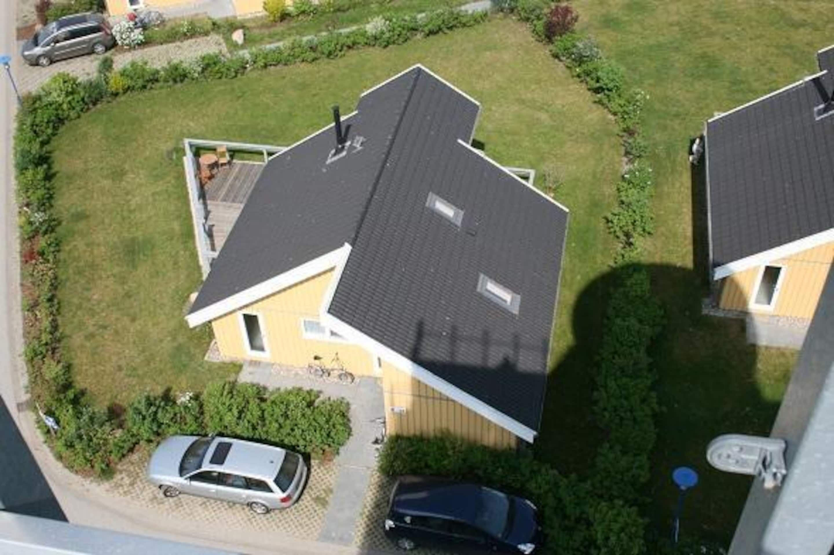 A residential area with two houses, each with a sloped roof and a small window. There are two cars parked in front of the houses, and a bicycle is visible near the left house.