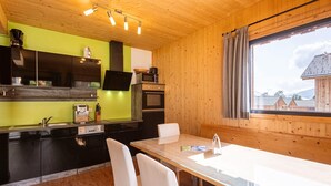 Cozinha moderna com teto de madeira, parede verde e área de jantar com mesa e cadeiras.