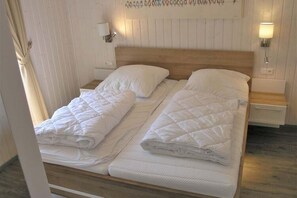 A double bed with white bedding, wooden headboard, bedside tables with lamps, and a wooden floor. - Ferienhaus im Ferienpark Mirow (Mirow)
