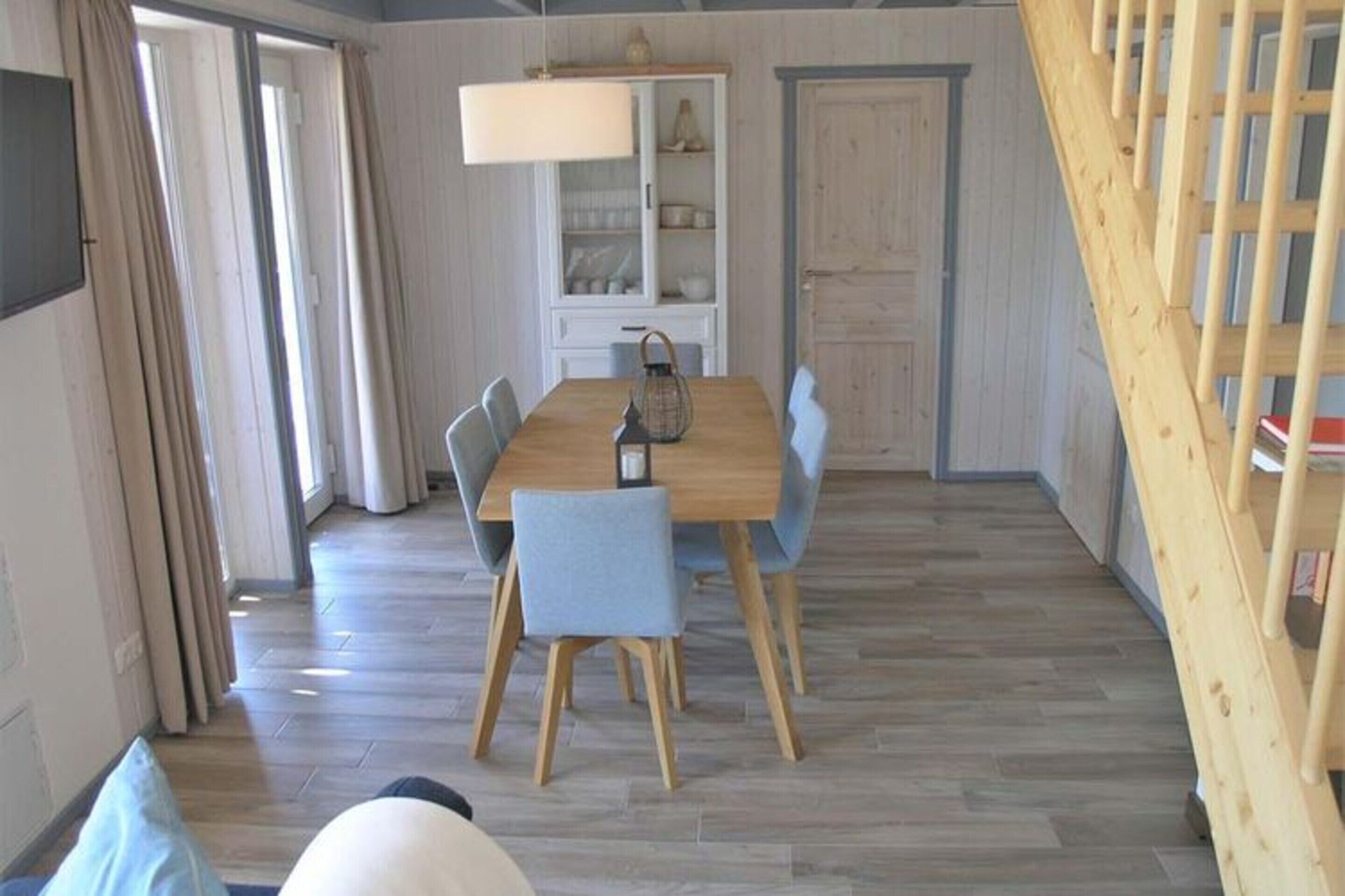 A dining area with a wooden table and chairs, a cabinet with dishes, and a staircase.