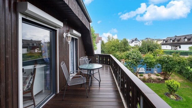 Een houten terras met een glazen deur, twee stoelen en een tafel.