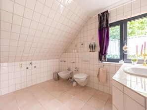 A bathroom with a toilet, bidet, and sink, tiled walls, and a window with curtains. - Ferienwohnung zum Zaubergarten (Birlenbach)