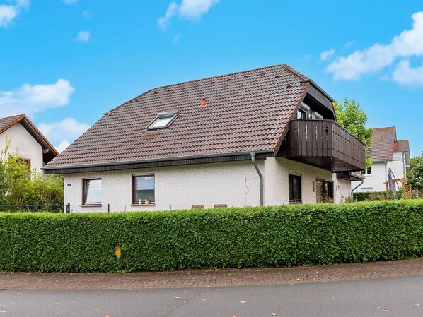 A two-story house with a sloped roof, a balcony on the upper floor, and a well-maintained hedge in front. - Ferienwohnung zum Zaubergarten (Birlenbach)