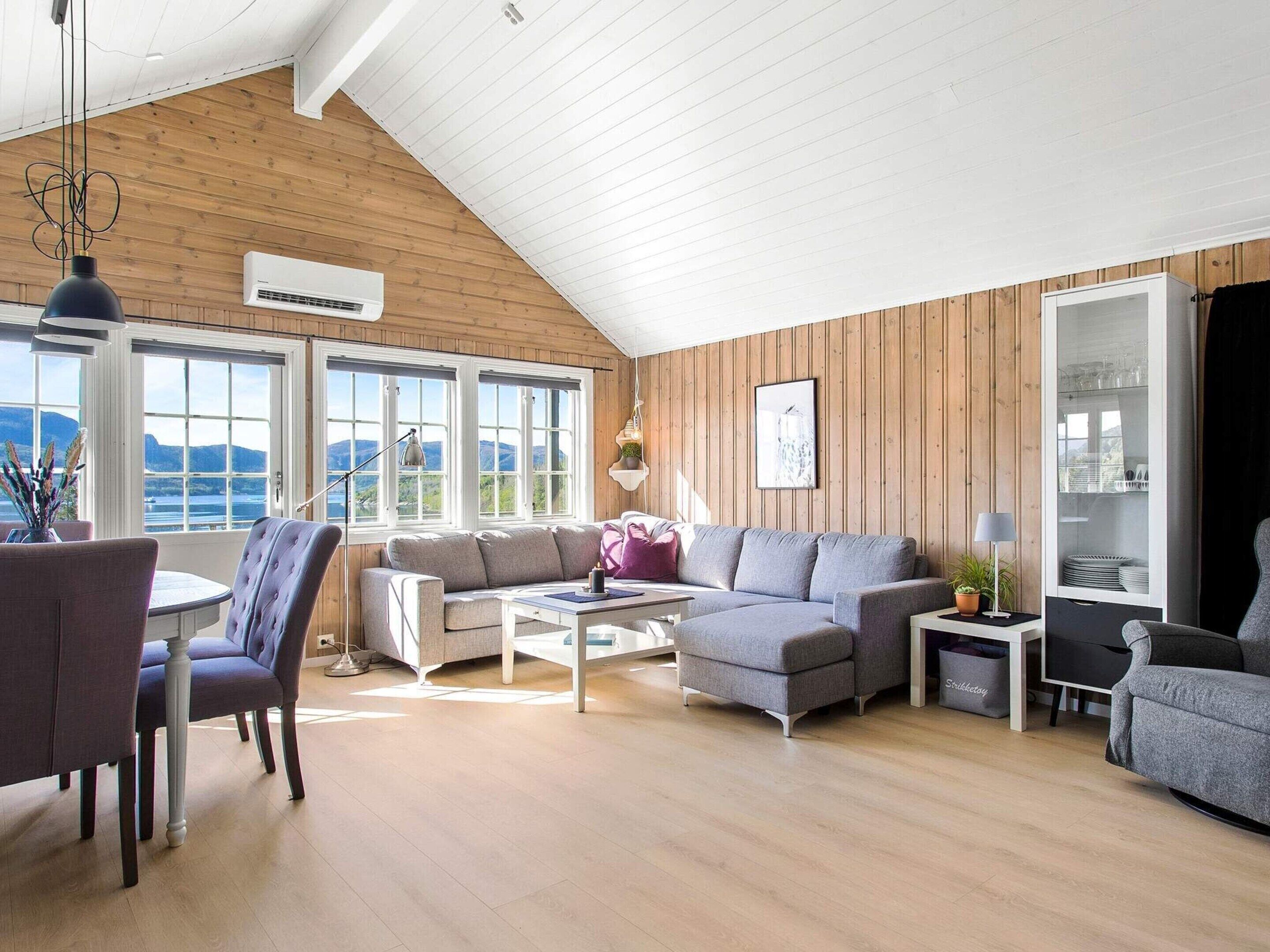 A spacious living area with a high ceiling, wooden walls, and large windows offering a view of the outdoors.