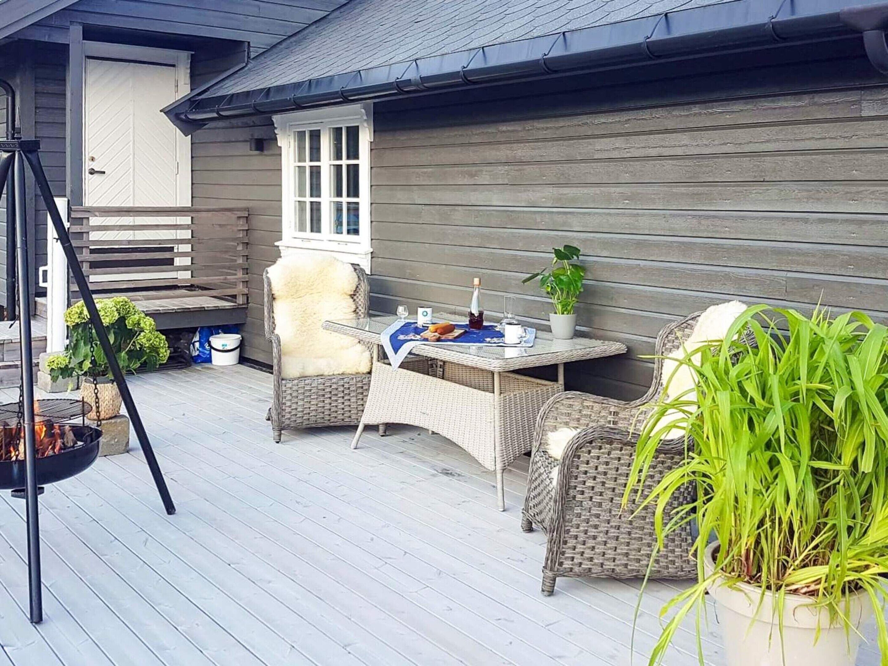 Un patio exterior con mobiliario de mimbre, una mesa con una botella y un vaso, y un brasero.