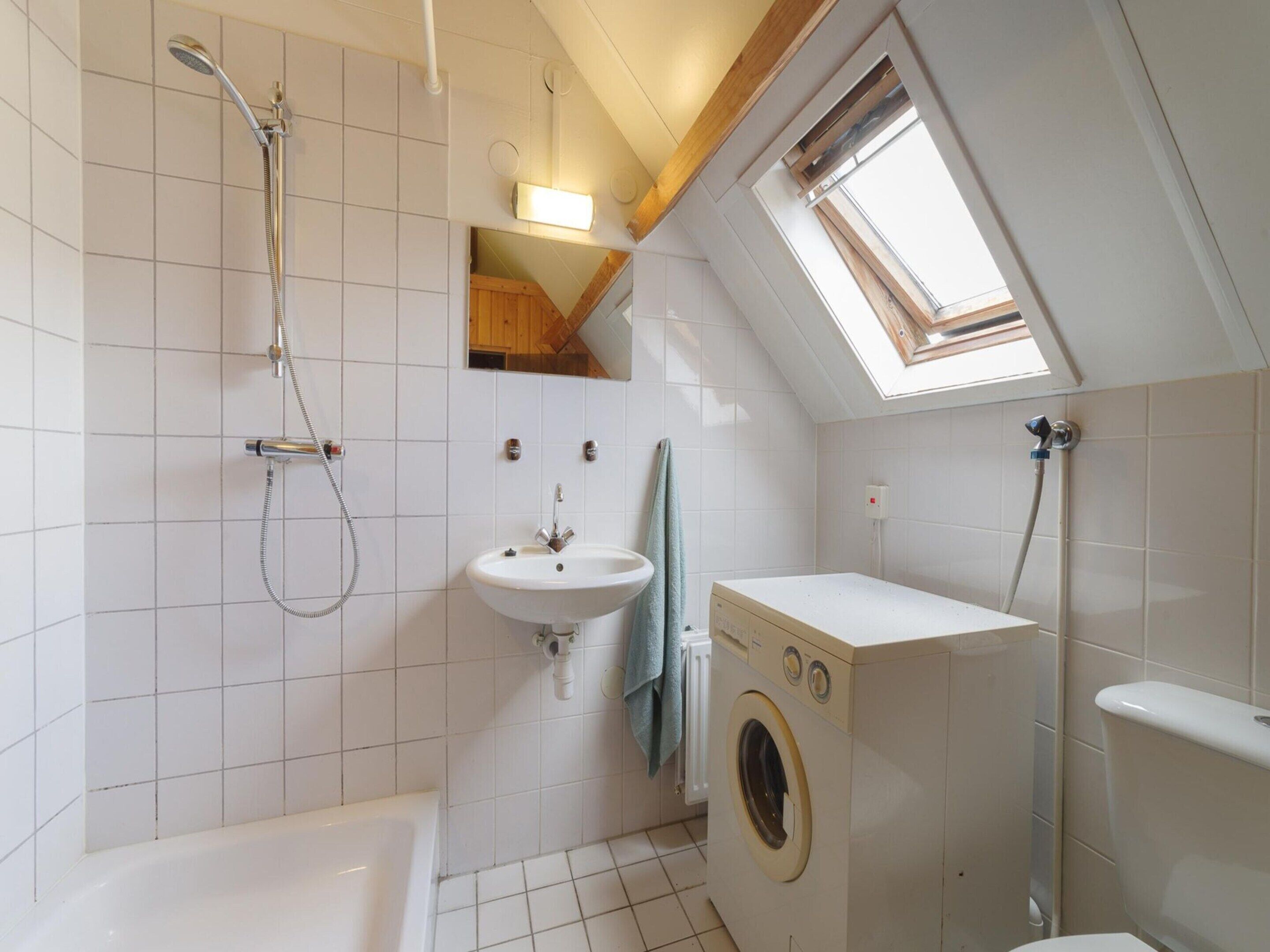 Ett litet badrum med badkar, handfat, tvättmaskin och dusch.