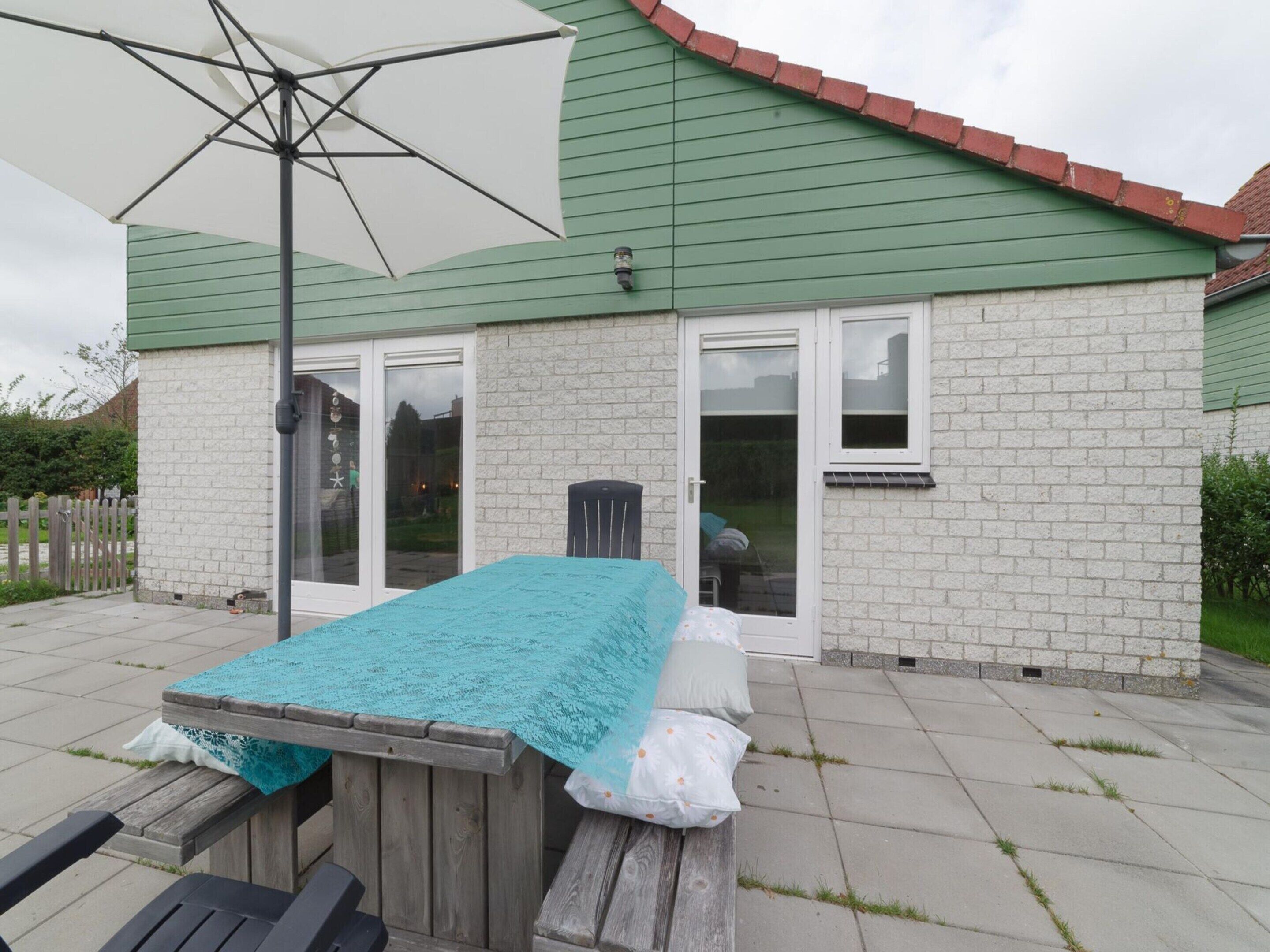 Eine Terrasse mit Holztisch, weißem Sonnenschirm und einem Ziegelhaus mit grüner Dachbegrünung.