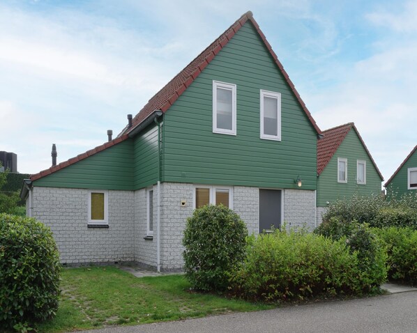 A two-story house with a green exterior and a red roof. It has a brick foundation and a small front porch. - Spacious Holiday Home With Sauna Near Beach (Wemeldinge)