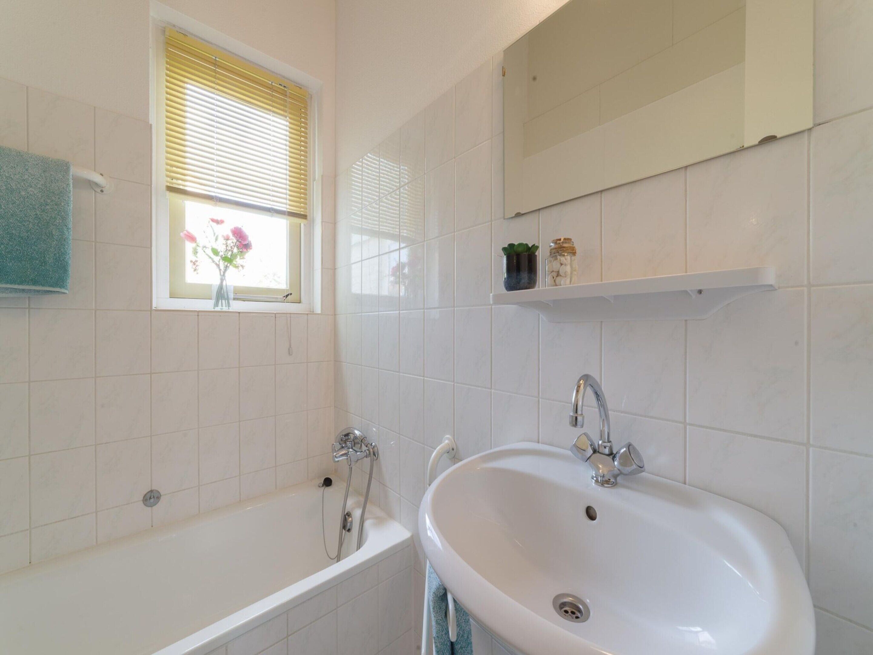 A bathroom with a bathtub, a sink, a window with flowers, and a mirror.