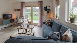 A living room with a sofa, a TV, a table with a vase, and a view of the garden through a sliding door. - Spacious Holiday Home With Sauna Near Beach (Wemeldinge)