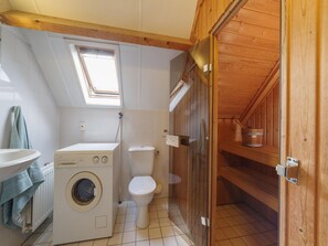 A compact, wooden-floored bathroom with a washing machine, toilet, and a small window. - Spacious Holiday Home With Sauna Near Beach (Wemeldinge)