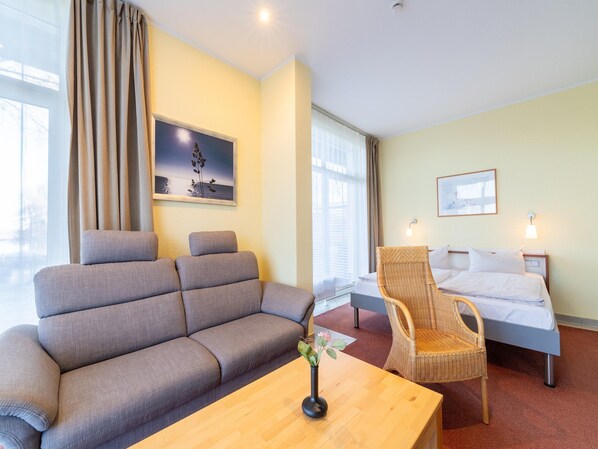 A hotel room with a sofa, a chair, a bed, and a wooden table.