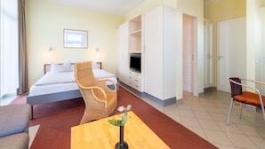 Ein Hotelzimmer mit einem Bett, einem Fernseher, einem Korbstuhl, einem Holztisch und einem Badezimmer mit Dusche und Toilette.