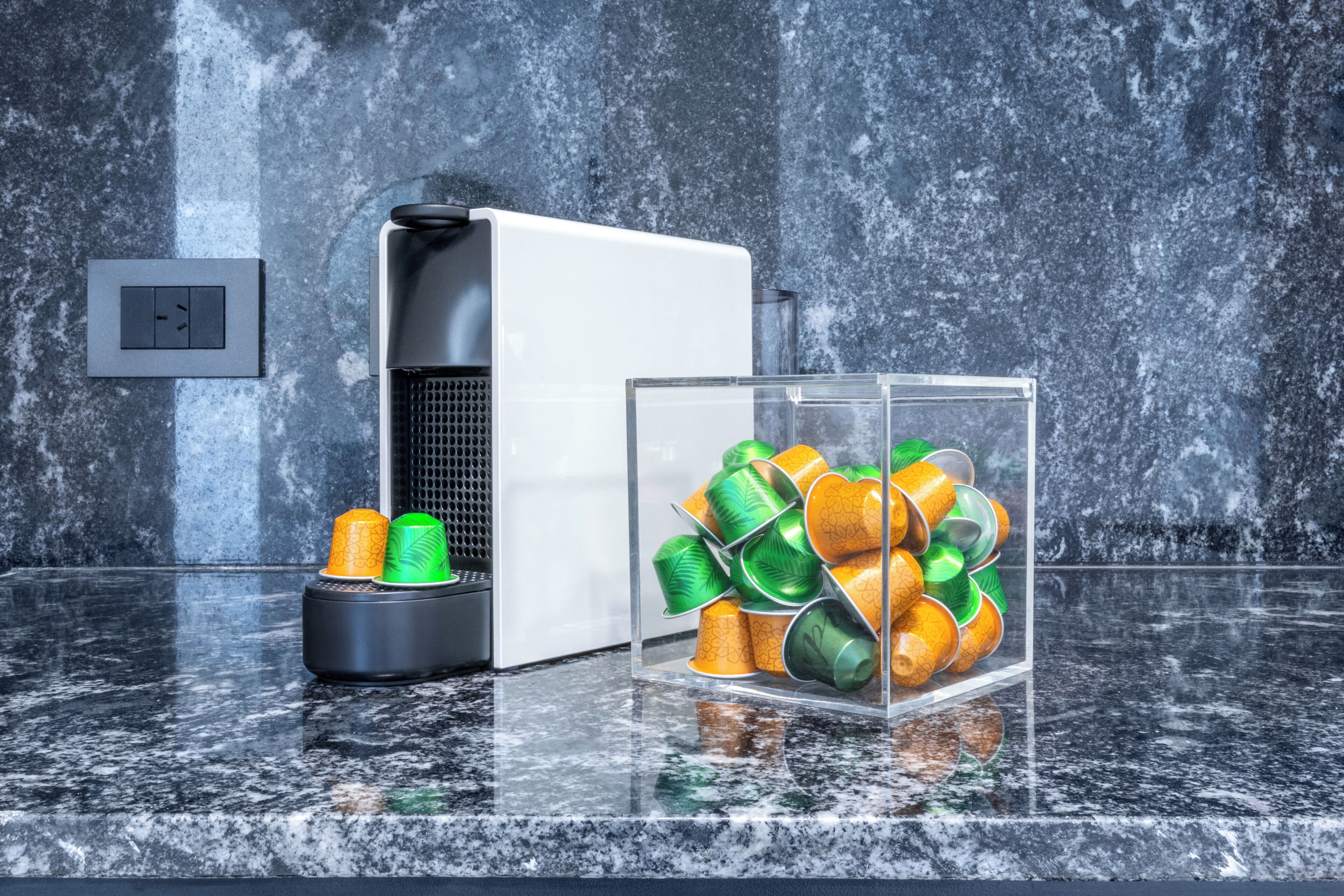 Eine Küche mit einem weißen Kühlschrank, einer schwarzen Kaffeemaschine und einem Glasbehälter mit grünen und gelben Tassen.