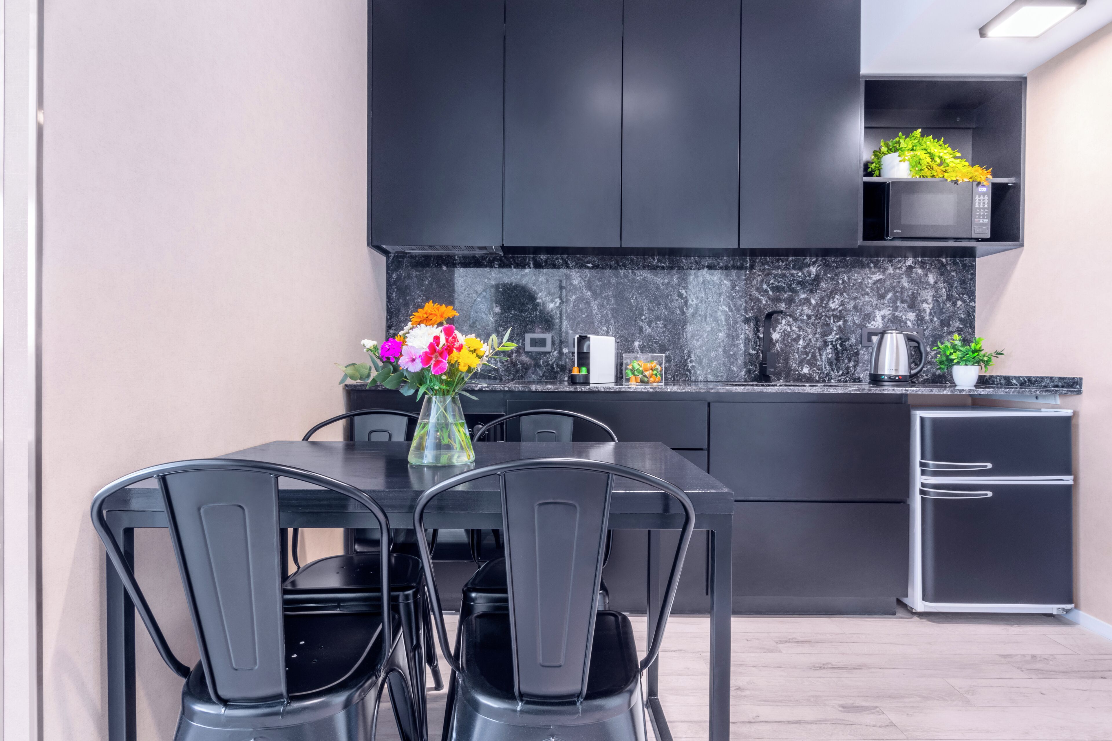 Una cocina moderna con armarios oscuros, encimera de mármol y una zona de comedor con sillas negras.