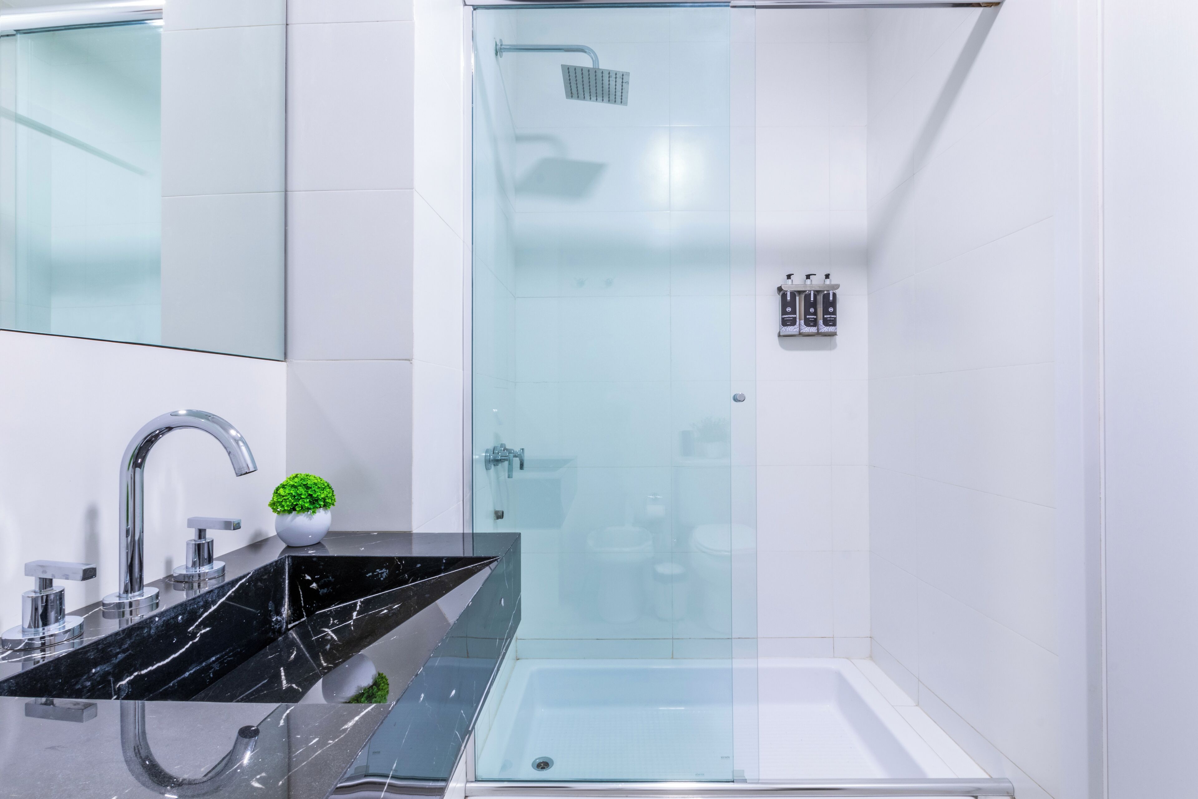 A modern bathroom with a glass-enclosed shower, a black marble sink, and a small potted plant.