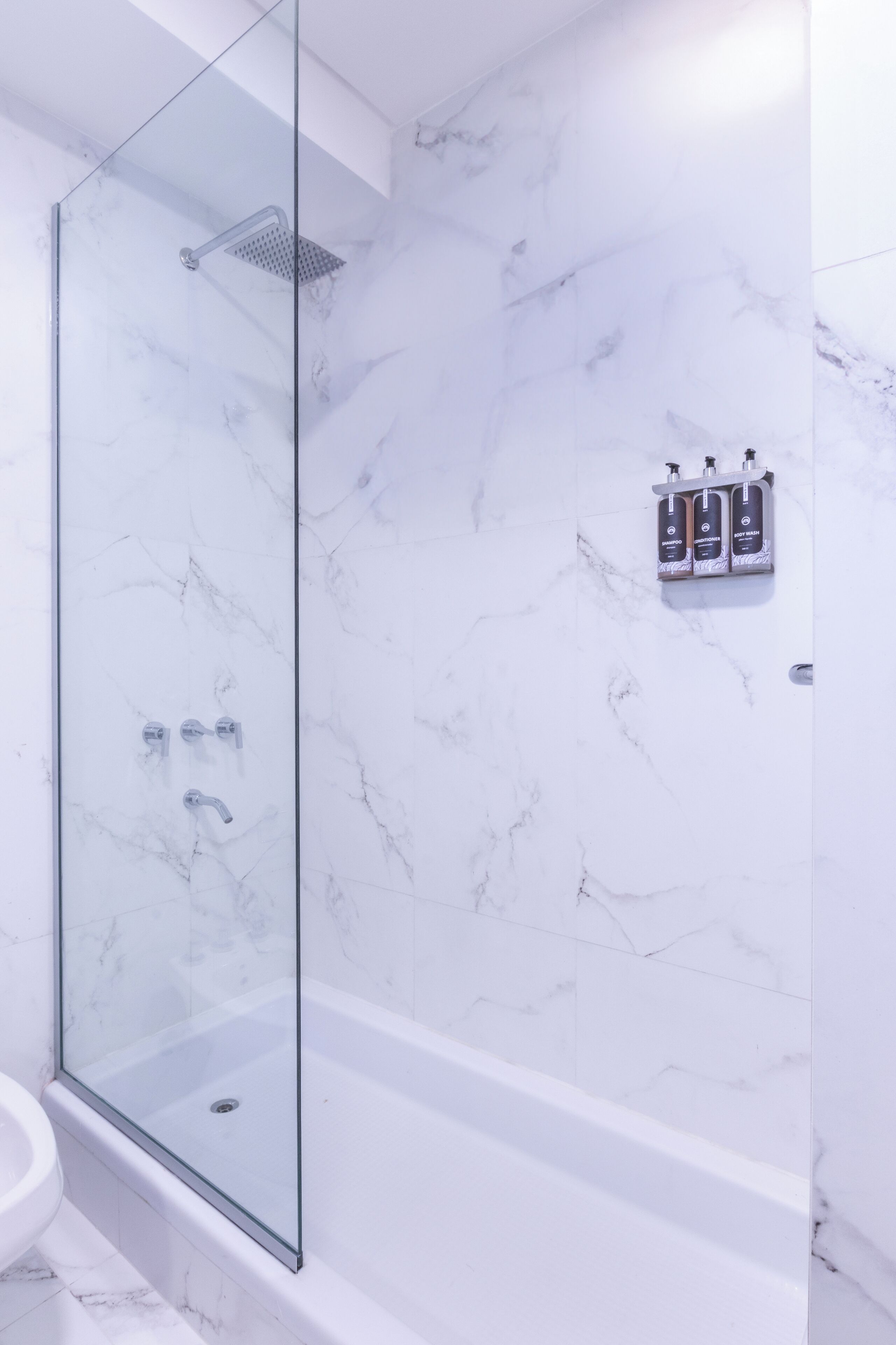 A modern bathroom with a glass-enclosed shower, a marble-tiled wall, and a built-in sink.