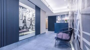 A modern lobby with a reception desk, a black chair, and a large window with a cityscape view.