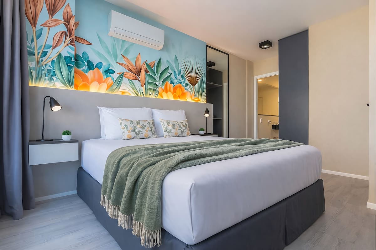 A modern bedroom with a bed, bedside tables, a green throw blanket, and a wall mural.